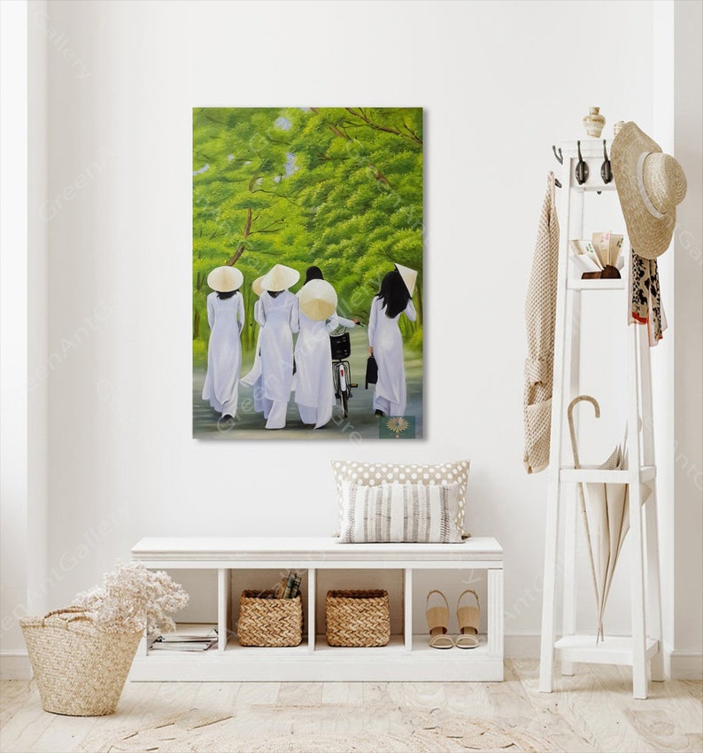 May include: A painting of four people wearing white ao dai dresses and conical hats walking down a path in a green forest. The people are walking in a line, and the person in the back is riding a bicycle.