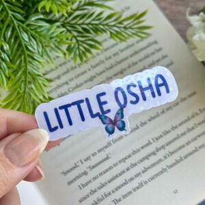 May include: A white sticker with a blue butterfly and the text "LITTLE OSHA" in blue lettering.