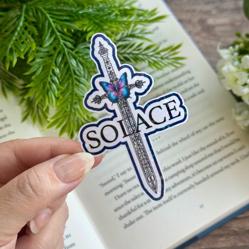 May include: A holographic sticker featuring a sword with a butterfly design and the word "SOLACE" in a white font.
