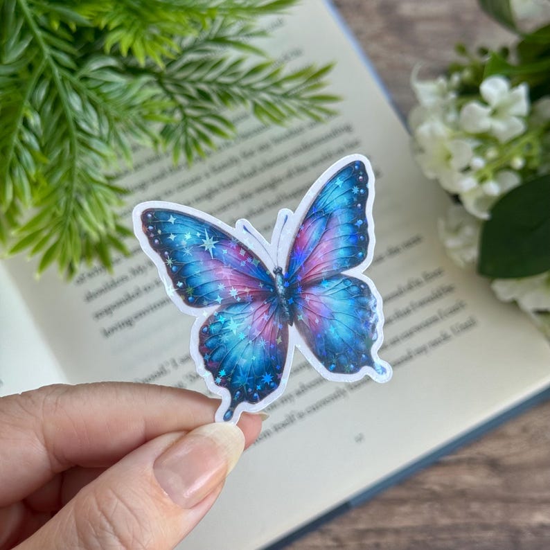May include: A blue and pink butterfly sticker with glitter accents. The butterfly has a detailed design with a galaxy-like pattern.