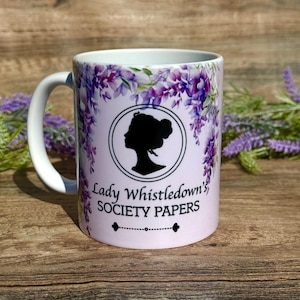 May include: White ceramic mug with a purple floral design and a silhouette of a woman's head. The text "Lady Whistledown's Society Papers" is printed on the mug.