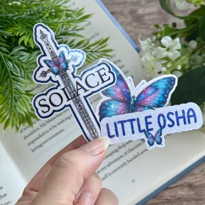 May include: Three stickers featuring a sword with a butterfly, a butterfly with glitter, and the text "SOLACE" and "LITTLE OSHA".