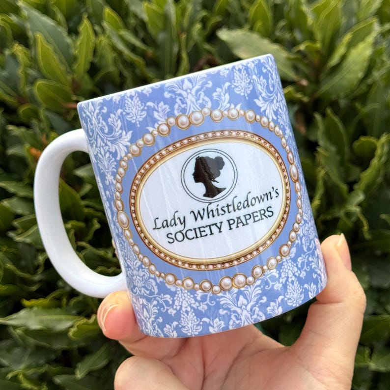 Puede incluir: Una taza de cer&aacute;mica blanca con fondo azul claro y estampado floral blanco. La taza presenta un dise&ntilde;o ovalado con una silueta y el texto "Lady Whistledown's SOCIETY PAPERS". El asa es blanca.