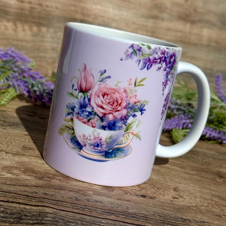 May include: A lavender-colored ceramic mug with a floral design. The design features a teacup filled with pink, purple, and blue flowers. The mug has a white handle.