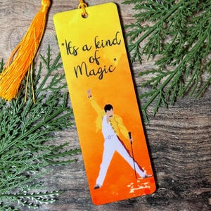 May include: A yellow bookmark featuring the text "It's a kind of Magic" and an illustration of a person in a yellow jacket and white trousers. The bookmark has an orange tassel attached.