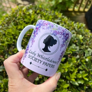 May include: White ceramic mug with a purple floral design and the text "Lady Whistledown's Society Papers" in black.