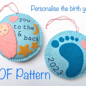 K&ouml;nnte beinhalten: Zwei Filz-Anh&auml;nger, einer blau mit einem Fu&szlig;abdruck und einem rosa Herz, der andere hellblau mit einem schlafenden Baby, Sternen, einem Mond und dem Text "you to the & back". Beide Anh&auml;nger haben eine rosa Schnur zum Aufh&auml;ngen und das Jahr "2023" ist auf dem blauen Anh&auml;nger geschrieben. Der Text "PDF Pattern" steht unter den Anh&auml;ngern.
