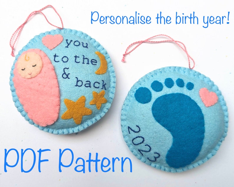 K&ouml;nnte beinhalten: Zwei Filz-Anh&auml;nger, einer blau mit einem Fu&szlig;abdruck und einem rosa Herz, der andere hellblau mit einem schlafenden Baby, Sternen, einem Mond und dem Text "you to the & back". Beide Anh&auml;nger haben eine rosa Schnur zum Aufh&auml;ngen und das Jahr "2023" ist auf dem blauen Anh&auml;nger geschrieben. Der Text "PDF Pattern" steht unter den Anh&auml;ngern.