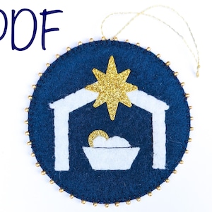 Peut inclure: Une décoration de Noël en feutre bleu avec une scène de crèche blanche et une étoile dorée pailletée. L'ornement est bordé de perles dorées et d'une ficelle dorée pour l'accrocher.