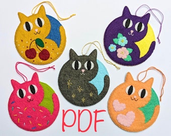 Könnte beinhalten: Fünf Filzkatzen-Anhänger mit verschiedenen Designs. Die Katzen sind in verschiedenen Posen, darunter sitzend, schlafend und zusammengerollt. Die Anhänger sind mit verschiedenen Farben und Mustern verziert, darunter Kirschen, Blumen und Sterne.