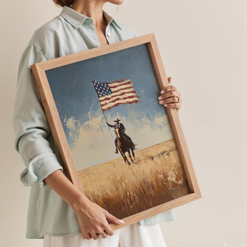 May include: A framed painting depicts a cowboy on horseback waving an American flag against a blue sky and golden field. The artwork is in a wooden frame.