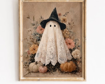 May include: A framed wall art print featuring a ghost draped in white lace fabric wearing a black pointed hat. The ghost is surrounded by a bouquet of muted-toned flowers in shades of pink, yellow, and cream, with two pumpkins at the base.
