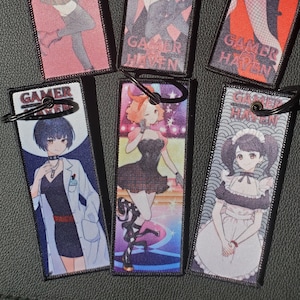 May include: Six rectangular keyrings with black metal hoops. Each keyring features a different anime-style character illustration with the text "GAMER HAVEN" at the bottom. The backgrounds are various colours, including pink, blue, and red.