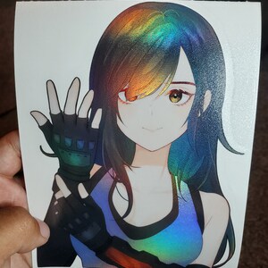 K&ouml;nnte beinhalten: Holografischer Aufkleber mit einem Anime-Charakter mit schwarzen Haaren und einem blauen und Regenbogenfarbschema. Die Figur tr&auml;gt ein blaues Oberteil und schwarze fingerlose Handschuhe. Der Aufkleber wird von einer Hand gehalten.