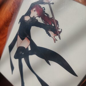 May include: A black and white illustration of a woman with long red hair holding a sword. She is wearing a black outfit with a long flowing skirt. The background is white.