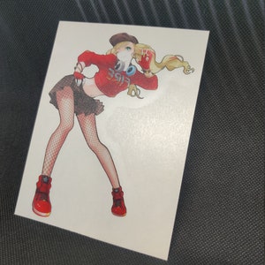 May include: A white sticker featuring a stylized anime-style illustration of a person in a red crop top with the word "Vibe" on it, a black skirt, and red sneakers. The person is wearing a brown hat and has blonde hair.