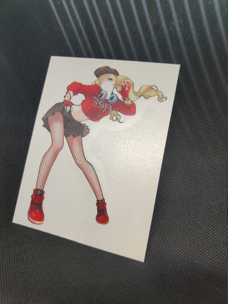 May include: A white sticker featuring a stylized anime-style illustration of a person in a red crop top with the word "Vibe" on it, a black skirt, and red sneakers. The person is wearing a brown hat and has blonde hair.