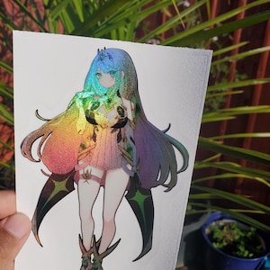 Può includere: Un adesivo olografico con un personaggio femminile di anime con lunghi capelli blu, che indossa un abito bianco e verde con una finitura iridescente arcobaleno. Il personaggio tiene un gioiello verde nelle sue mani.