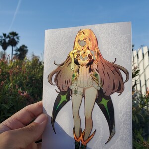May include: A holographic sticker featuring a female anime character with long brown hair, wearing a white and green outfit with gold accents. The character is standing with her arms crossed and has a serious expression.