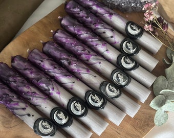 May include: A set of ten purple and silver candles with black wax seals. Each seal features a crescent moon and a sprig of leaves.