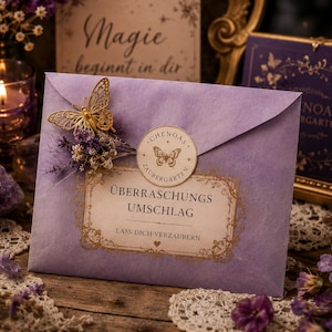 Könnte beinhalten: Ein hellvioletter Umschlag mit einer goldenen Schmetterlingsverzierung, getrockneten violetten Blumen und einem runden Siegel mit Schmetterlingssymbol. Das Etikett trägt die goldene Aufschrift "CHENOAS ZAUBERGARTEN", "ÜBERRASCHUNGS UMSCHLAG" und "LASS DICH VERZAUBERN".