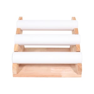 May include: A three-tiered jewelry display stand. The stand is made of light-colored wood and features three white, cylindrical bars for displaying bracelets or bangles. The design is simple and functional, with a clean aesthetic.