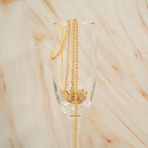 K&ouml;nnte beinhalten: Eine goldene Kettenkette, die in einer klaren Glas-Champagnerfl&ouml;te drapiert ist.