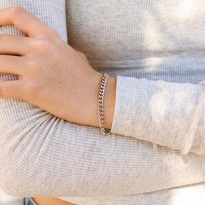 K&ouml;nnte beinhalten: Ein silbernes Kettenarmband mit einem Gliederketten-Design. Das Armband wird am Handgelenk getragen.