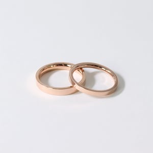 May include: Two simple rose gold wedding bands, one slightly larger than the other, are shown on a white background.