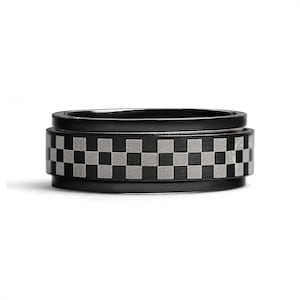 May include: A black spinning ring with a checkered pattern. The ring is made of metal and has a smooth finish.