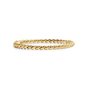 May include: A gold-colored ring with a twisted rope design. The ring is a thin band, and the rope pattern wraps around the entire circumference. The ring is set against a plain white background, highlighting its metallic sheen.