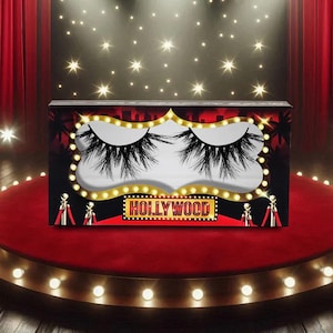 May include: A box of black false eyelashes with a Hollywood theme. The box features a red and black design with the word "HOLLYWOOD" in gold lettering. The eyelashes are displayed against a white background.
