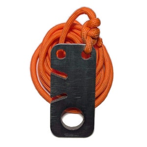 May include: A black metal fire starter with a hole and a serrated edge, attached to an orange paracord.
