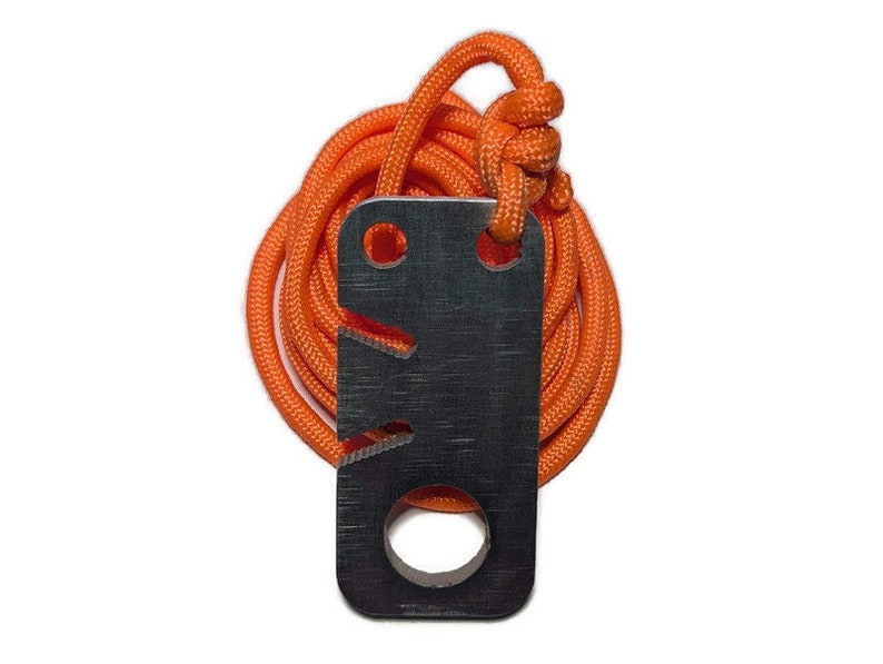 May include: A black metal fire starter with a hole and a serrated edge, attached to an orange paracord.