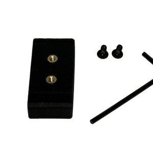 Può includere: Un componente rettangolare nero con due fori per viti color oro, due piccole viti nere e una chiave a brugola nera. Gli elementi sono disposti su sfondo bianco.