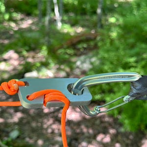 May include: A silver metal camping gear attachment with a carabiner and orange rope. The carabiner has the text "Not for Climbing Use" engraved on it.