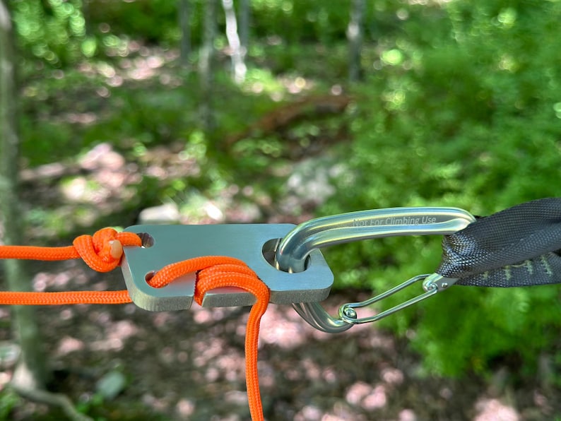 May include: A silver metal camping gear attachment with a carabiner and orange rope. The carabiner has the text "Not for Climbing Use" engraved on it.