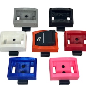 Könnte beinhalten: Sortiment von sieben 3D-gedruckten Kunststoff-Kippschaltern in verschiedenen Farben, darunter Grau, Schwarz, Weiß, Orange, Rot, Blau und Pink. Der orange Schalter hat den Text "fi" aufgedruckt.