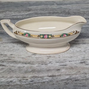 May include: A white ceramic gravy boat with a gold trim and pink and green floral design.