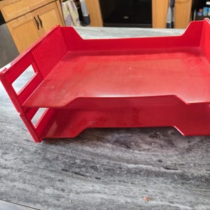 May include: A red plastic two-tiered file tray with a smooth surface.