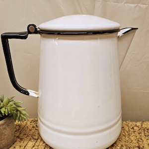 May include: White enamelware coffee pot with a black handle and rim. The vintage pot has a lid and a spout for pouring. The coffee pot is a classic kitchenware item.