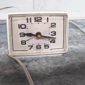 May include: A white analog alarm clock with black numbers and hands. The clock face reads "Westclox" and "Made in U.S.A."