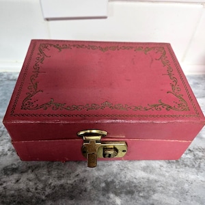 May include: A pink jewelry box with a gold latch and a decorative gold border. The box has a vintage look.
