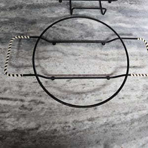 May include: Black metal cake stand with a white and black striped handle. The stand is round and has a raised edge.