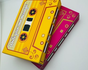 Könnte beinhalten: Zwei übereinander gestapelte Boxen mit einem Retro-Kassettenband-Design. Die obere Box ist gelb mit dem Text "Write your own message" und die untere Box ist pink mit goldenen Akzenten.