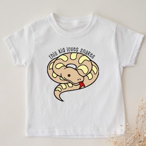 May include: White t-shirt featuring a cartoon snake design with the text "this kid loves snakes." The snake is tan with yellow markings and a red tongue. The shirt is a short-sleeved crew neck.