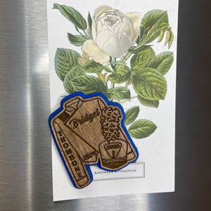 May include: A wooden cutout of a trombone player in a marching band uniform. The cutout is painted blue and brown and has the text "Bridget Trombone 2024 SVMS Baroness Rothschild" engraved on it.