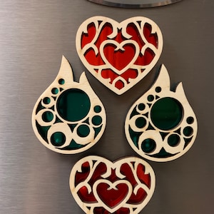 K&ouml;nnte beinhalten: Vier Holzornamente mit komplizierten Designs. Zwei sind herzf&ouml;rmig mit roten Glaseins&auml;tzen und zwei sind flammenf&ouml;rmig mit gr&uuml;nen Glaseins&auml;tzen.
