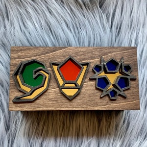 May include: A wooden sign with three different colored geometric shapes. The shapes are outlined in black and have a gold interior. The shapes are green, red, and blue.