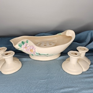 以下が含まれることがあります： 4つのヴィンテージセラミックキャンドルホルダーと花の中心部のセット。キャンドルホルダーは白で、テクスチャ加工が施され、ユニークなデザインです。中心部は、花用の穴が中央にある花柄の白いボウルです。
